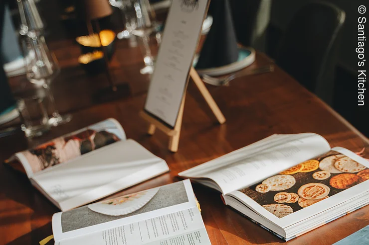 Kochinspiration Brauner Tisch mit fünf aufgeschlagenen Kochbüchern und einer Menükarte