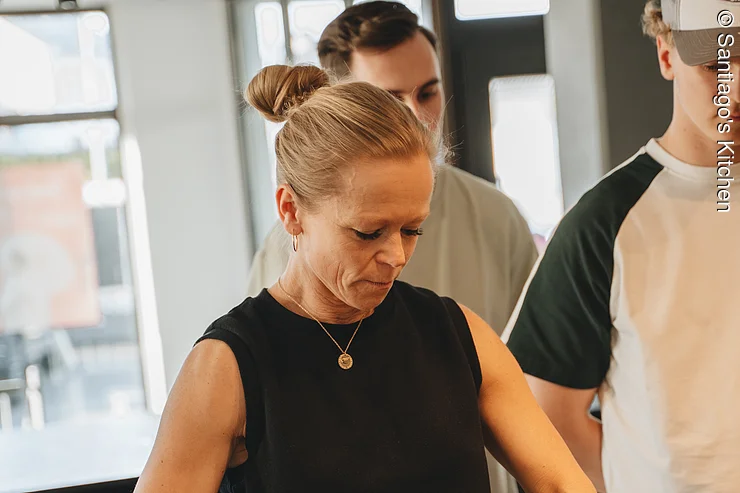 Teambuilding Kochkurs Frau bereitet Essen zu und zwei weitere Personen schauen zu