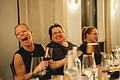 Drei lachende Personen sitzen Weintrinkend an einem Tisch