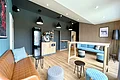 Loungebereich mit zwei Sofas, mehreren Sitzhöckern, Beistelltischen und einem Stehtisch. An der Wand gibt es eine Kaffeeecke mit einem Getränkekühlschrank.