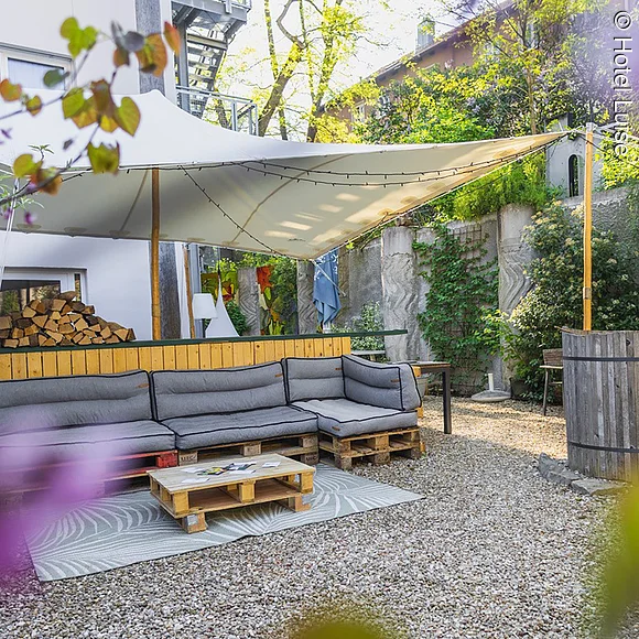 Tiefhof Innenhof mit Loungemöbeln, Sonnenschirm, kleiner Bar und vielen Blumen.