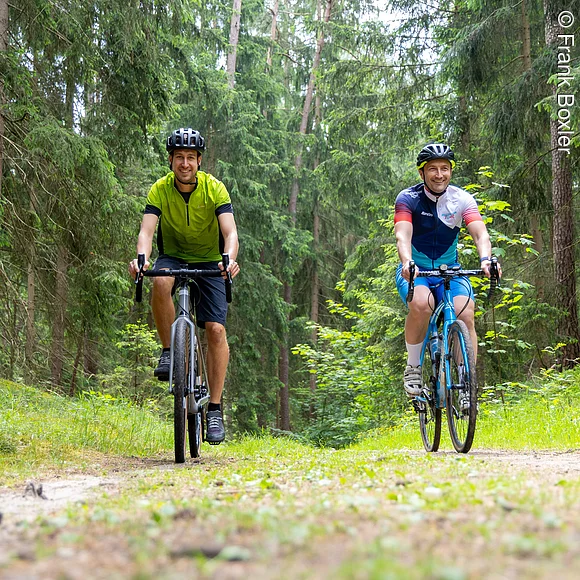 Zwei Gravelbiker fahren durch Waldstück