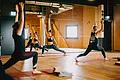 Drei Personen machen Sportübungen auf Yogamatten in einem Fitnessraum mit Spiegel