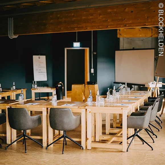 Moderner Eventraum mit Holztischen, schwarzen Stühlen und Seminarausstattung