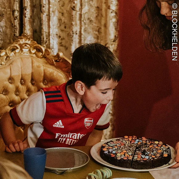 Junge sitzt auf einem Thron und feiert Geburtstag. Frau bringt Schokokuchen an den Tisch.