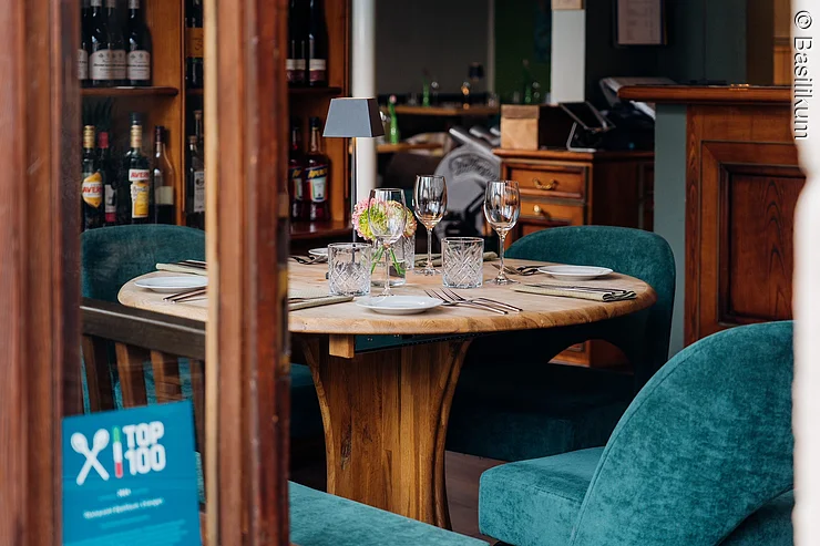 kleiner runder gedeckter Holztisch, davor Sessel in Türkis