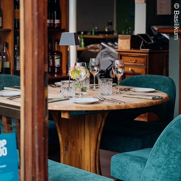 Restaurant Basilkim kleiner runder gedeckter Holztisch, davor Sessel in Türkis