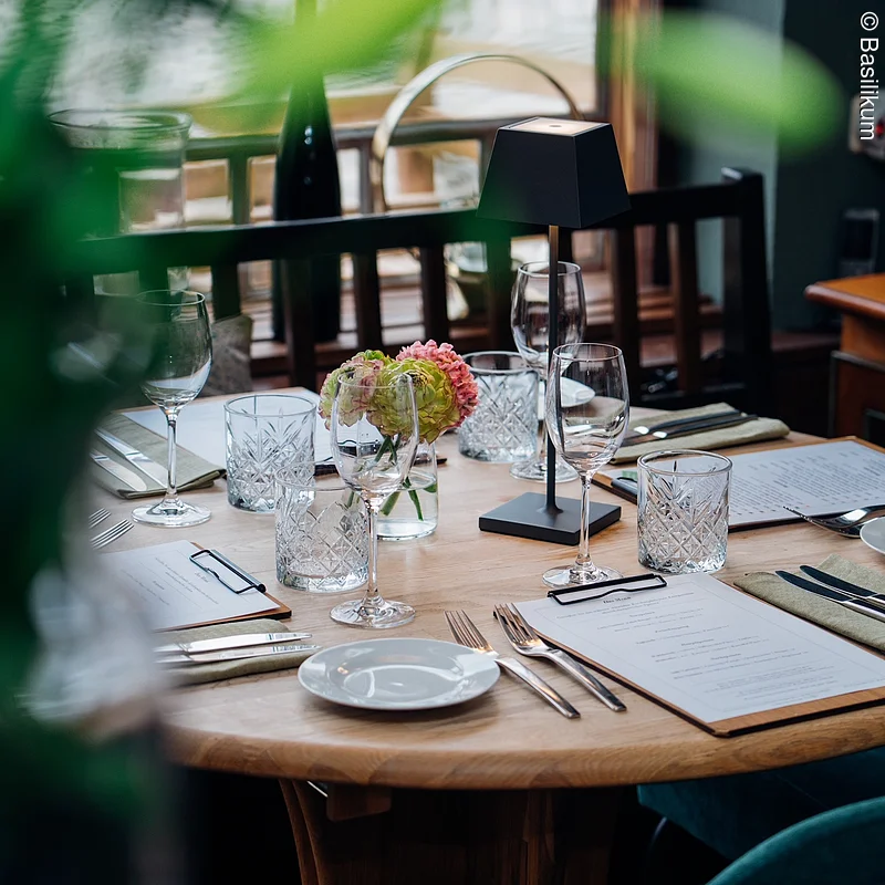 gedeckter Tisch am Fenster, vorne unscharf Pflanze