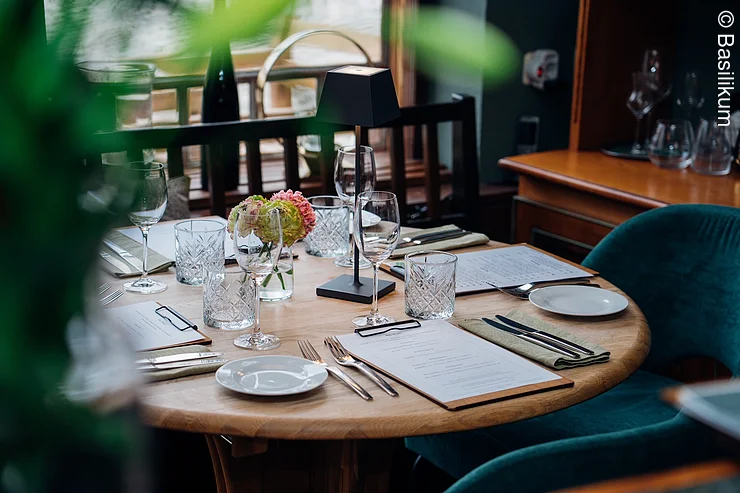 gedeckter Tisch am Fenster, vorne unscharf Pflanze