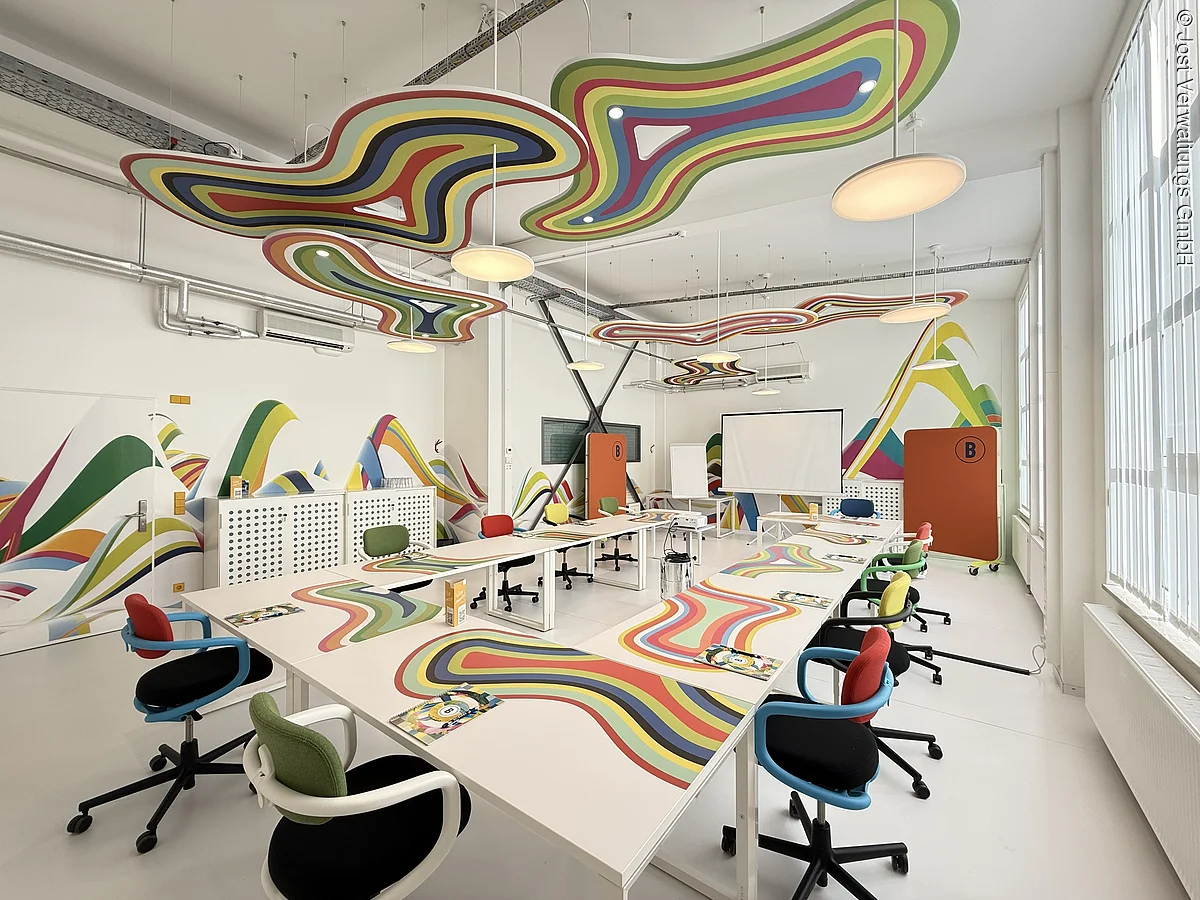 عناصر تصميمية ملونة تُزيّن السقف والطاولات والجدران. الطاولات مُرتّبة على شكل حرف U.