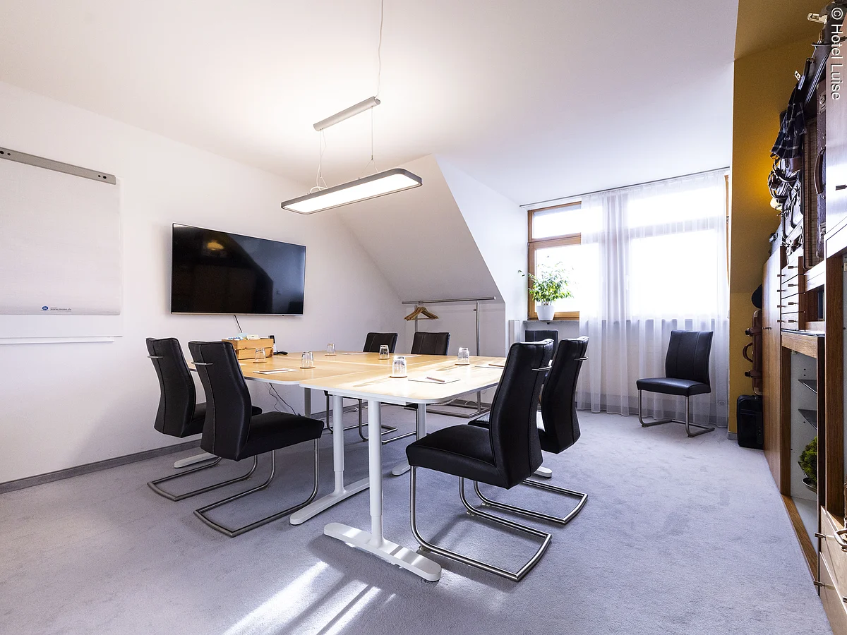 kleiner Tagungsraum mit Gruppentisch und verschiedenen alten Koffern als Dekoartikel im Regal an der Wand.