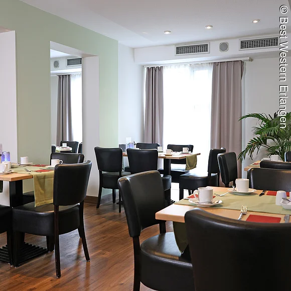 Raum mit kleinen Tischen, eingedeckt für Frühstück.