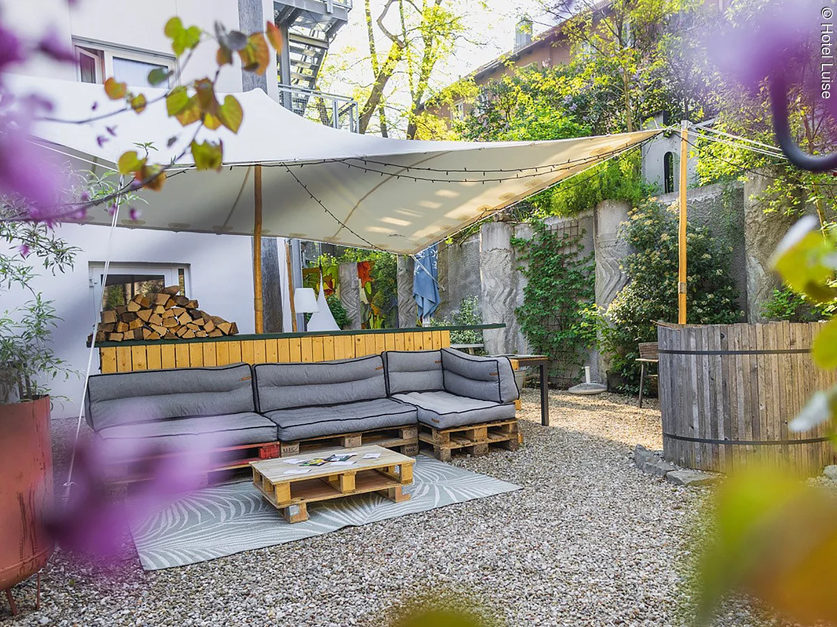 Innenhof mit Loungemöbeln, Sonnenschirm, kleiner Bar und vielen Blumen.